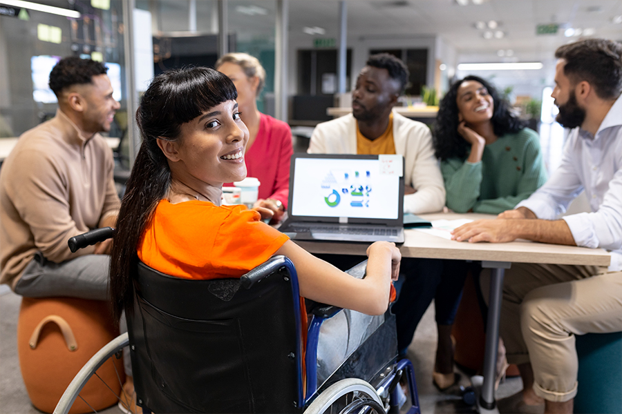 Mujer con diversidad funcional en silla de ruedas participando en una reunión de trabajo inclusiva, representando empresas que rompen barreras laborales.